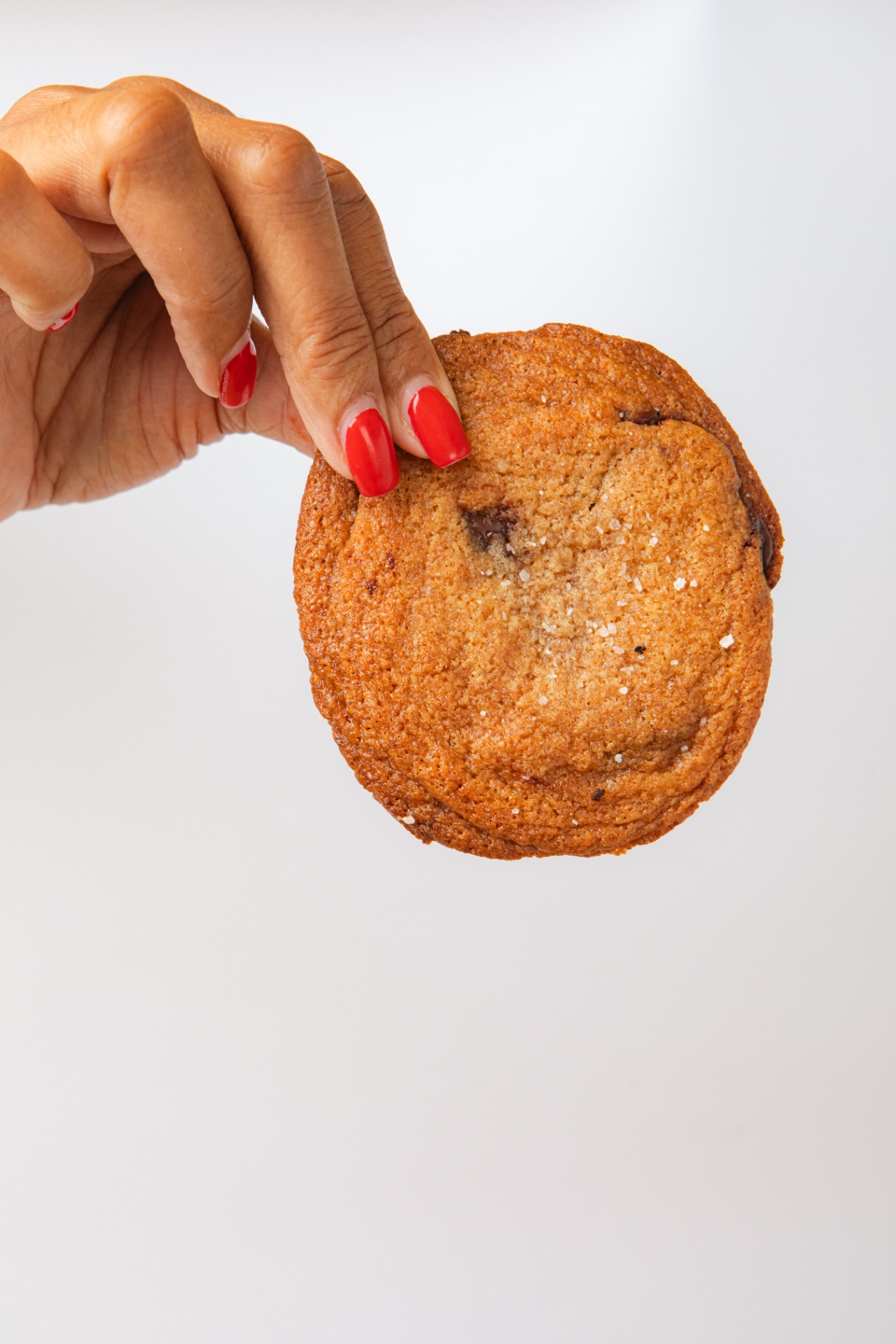 A hand holding a thin, crispy Chippies chocolate chip cookie
